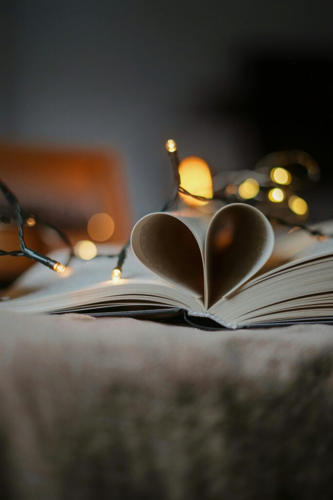 A close-up of a book with pages folded into a heart shape, adorned with glowing fairy lights.