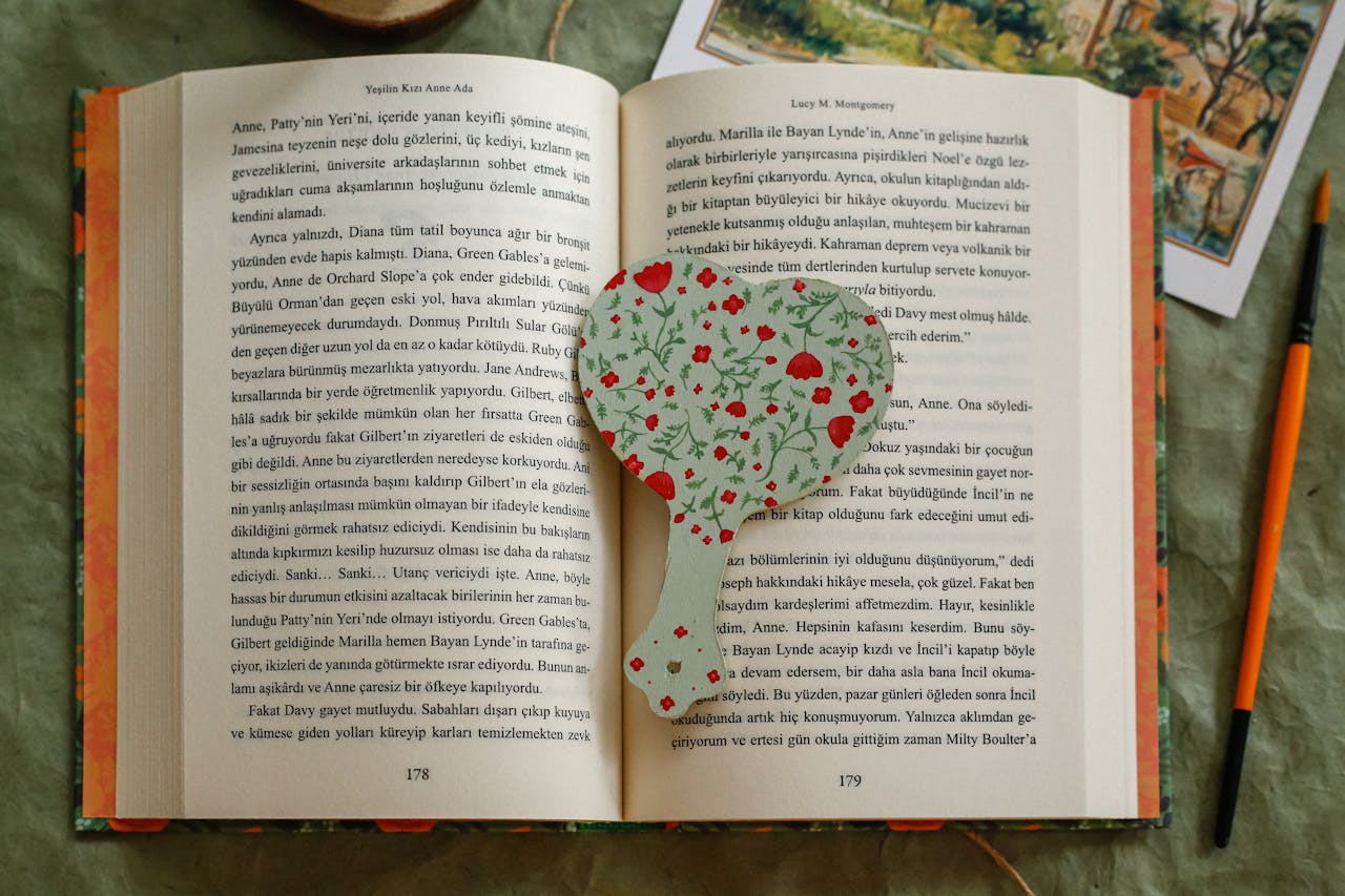 A heart-shaped floral bookmark lies on an open Turkish book, creating a cozy reading scene.