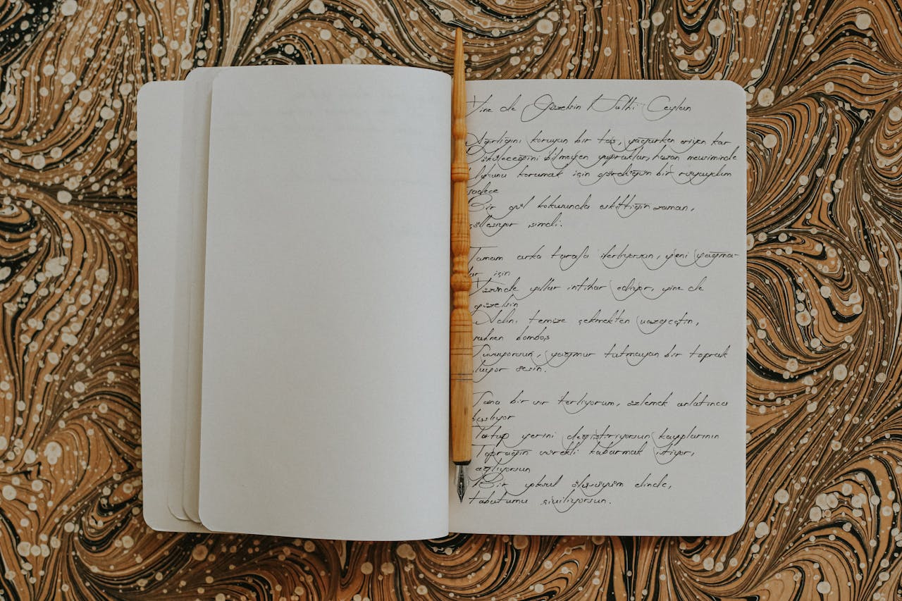 Open notebook showcasing calligraphy with a wooden pen on a brown marbled surface.